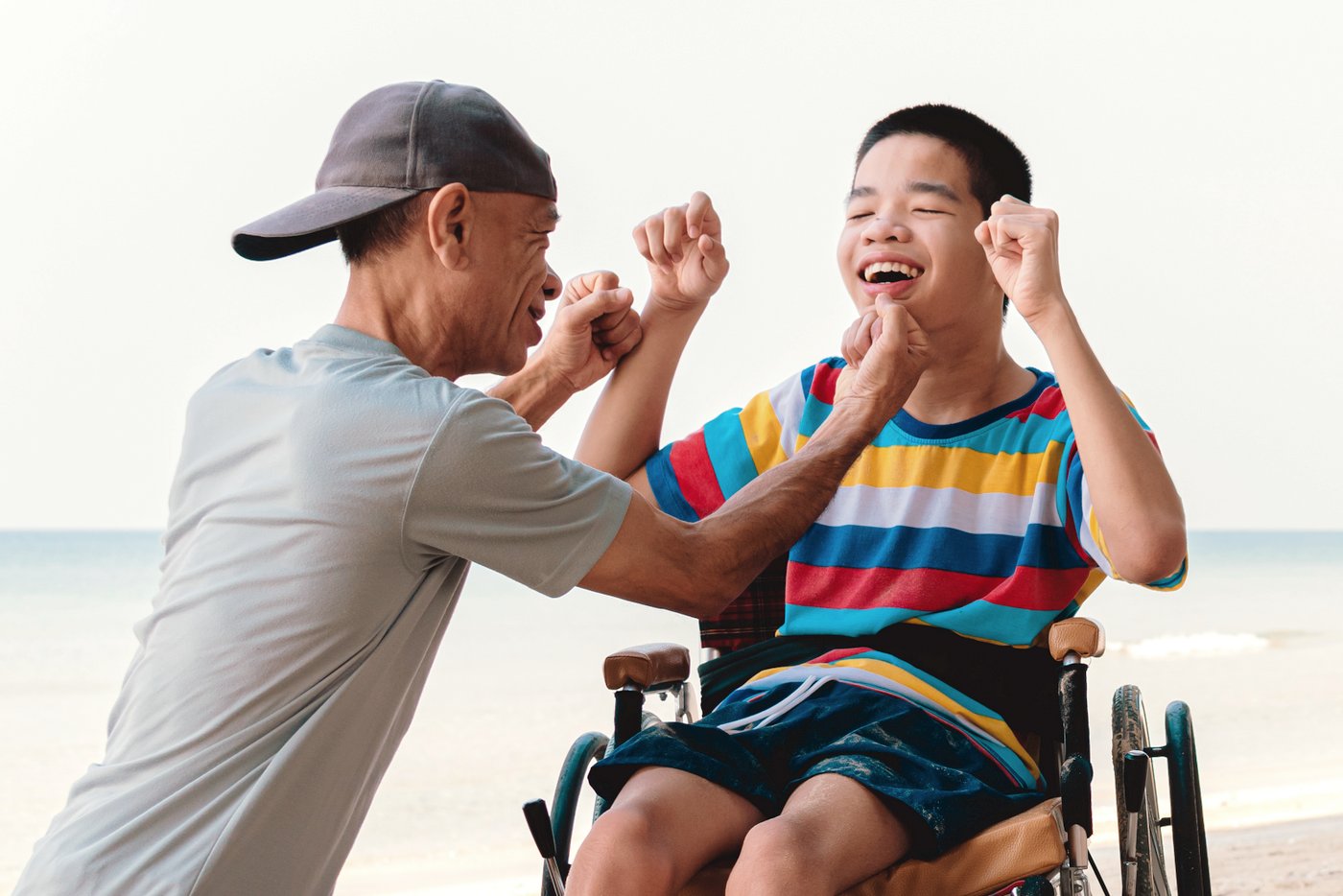 Boy in a wheelchair and his father at the beach