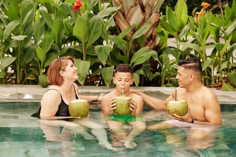 Family vacation - Parents and child in a swimming pool drinking from coconuts