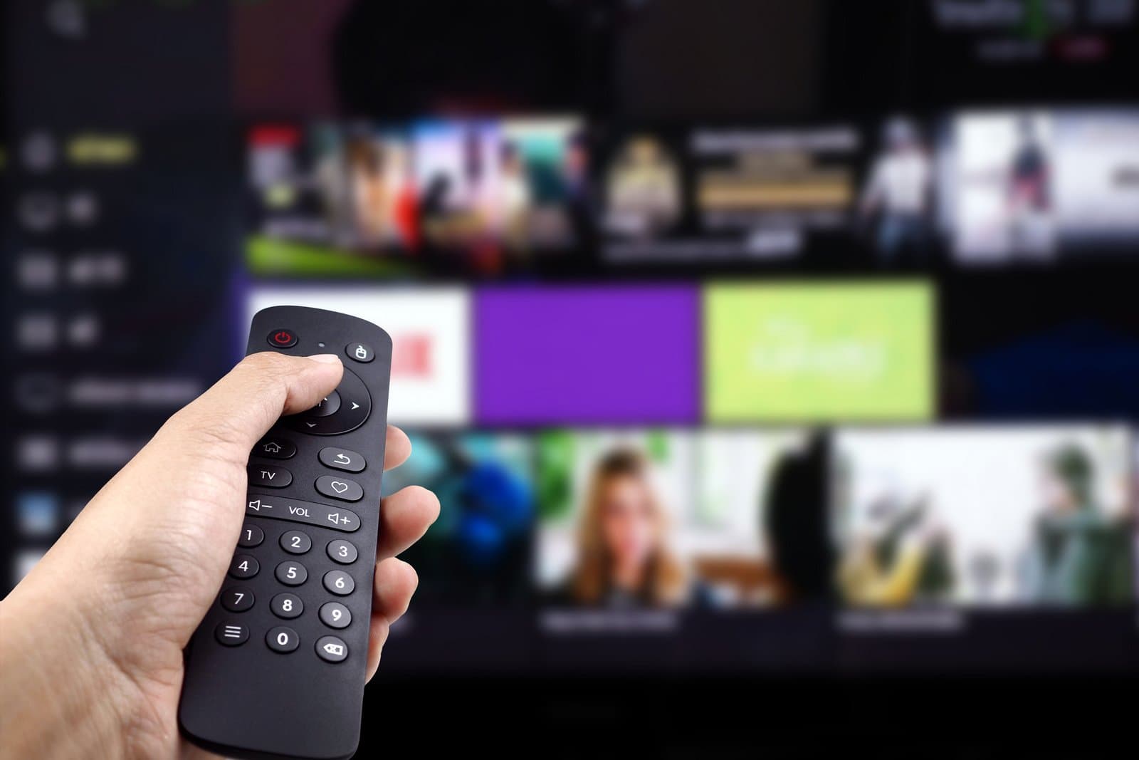 Hand holding TV remote control for on-demand binge watching streaming services