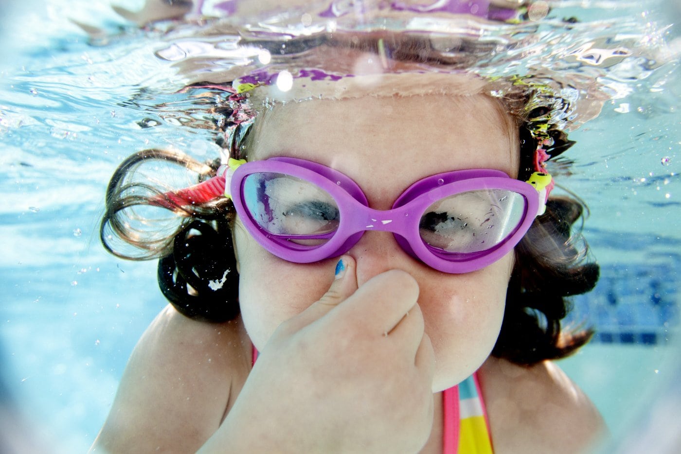 Little girl in swim goggles underwater in a pool