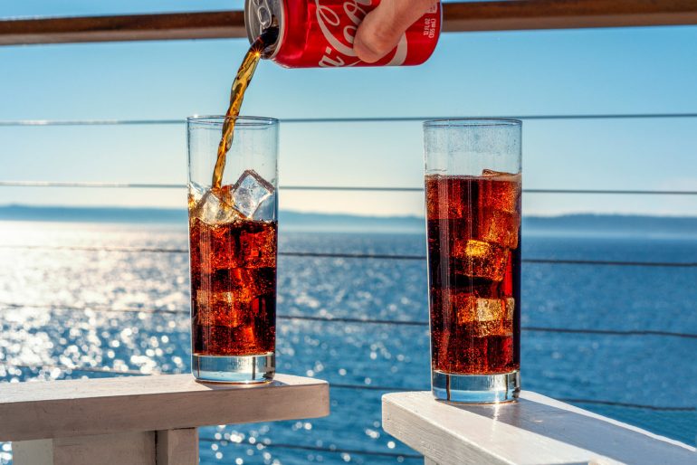 Pouring cold cola soda from a can into tall glasses
