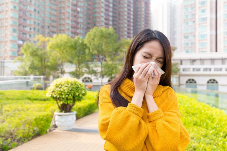 Sneezing woman with allergies outdoors in spring