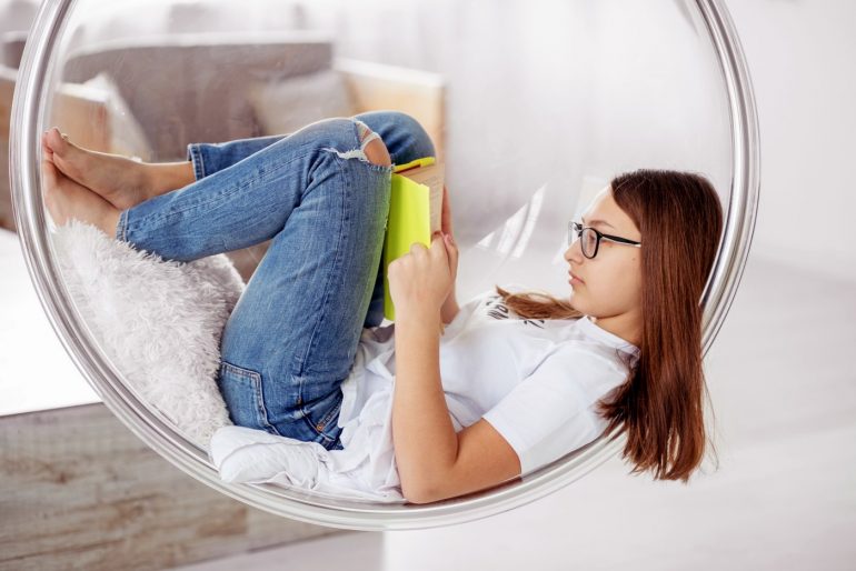 Teen girl reading a book in a retro swinging chair