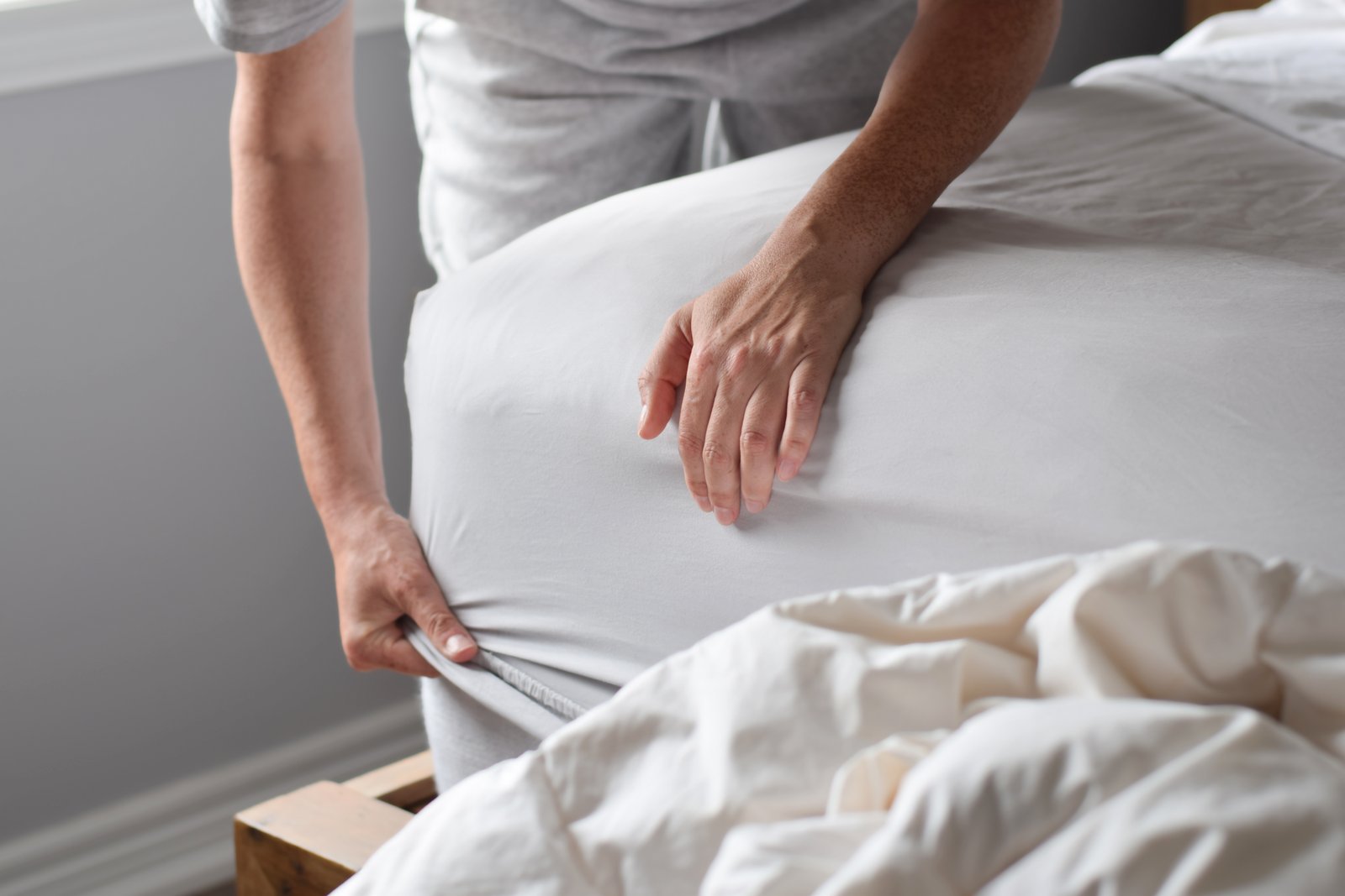 Woman putting a white fitted sheet on a bed