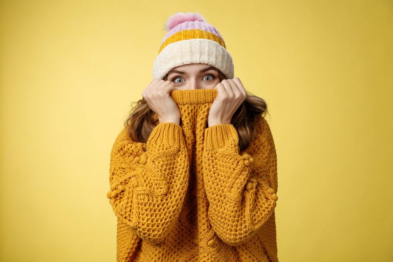 Woman wearing a sweater and hat hiding her face
